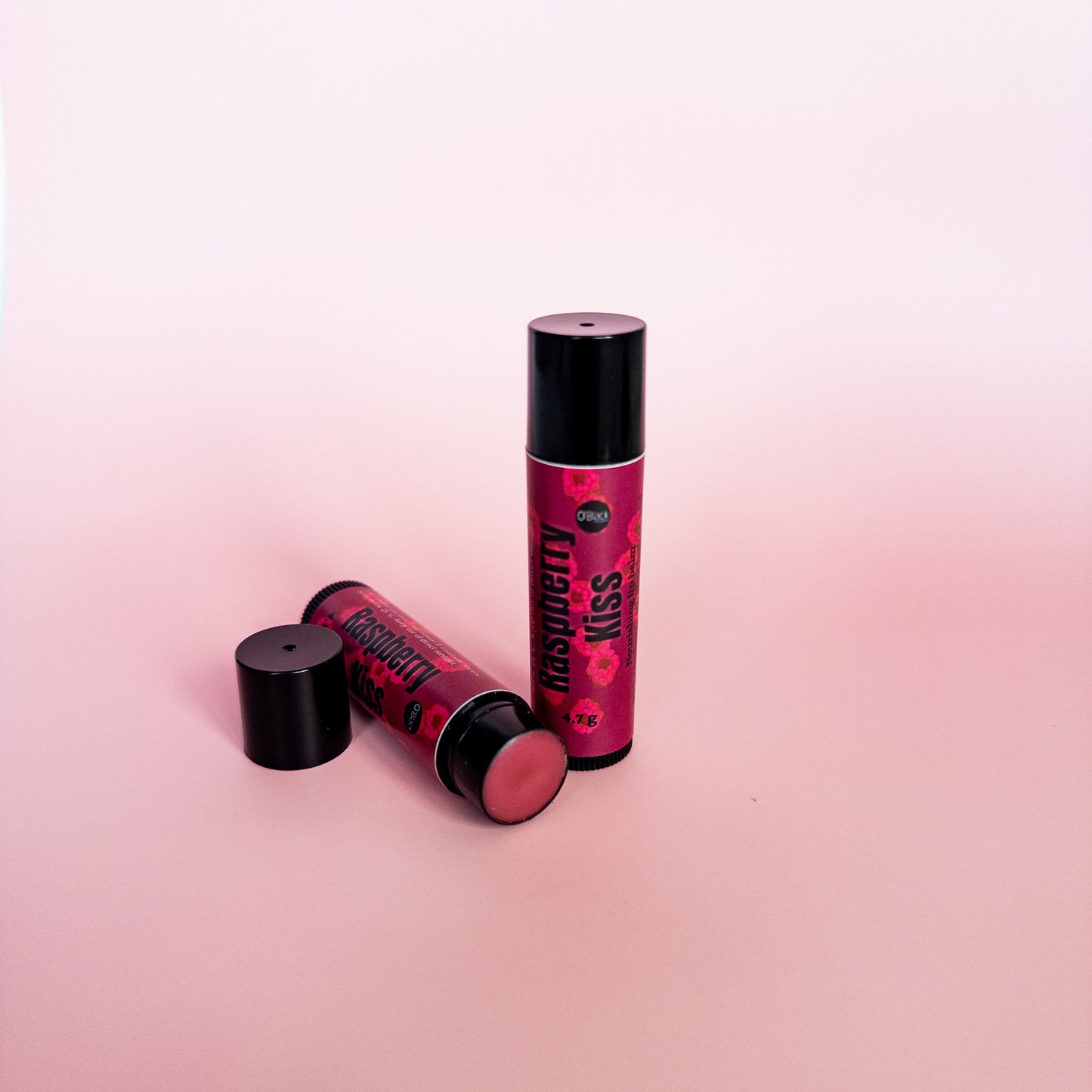 Two lip balm tubes labeled 'Raspberry Kiss' on a pink background