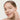 Woman applying cream to her face on a plain background