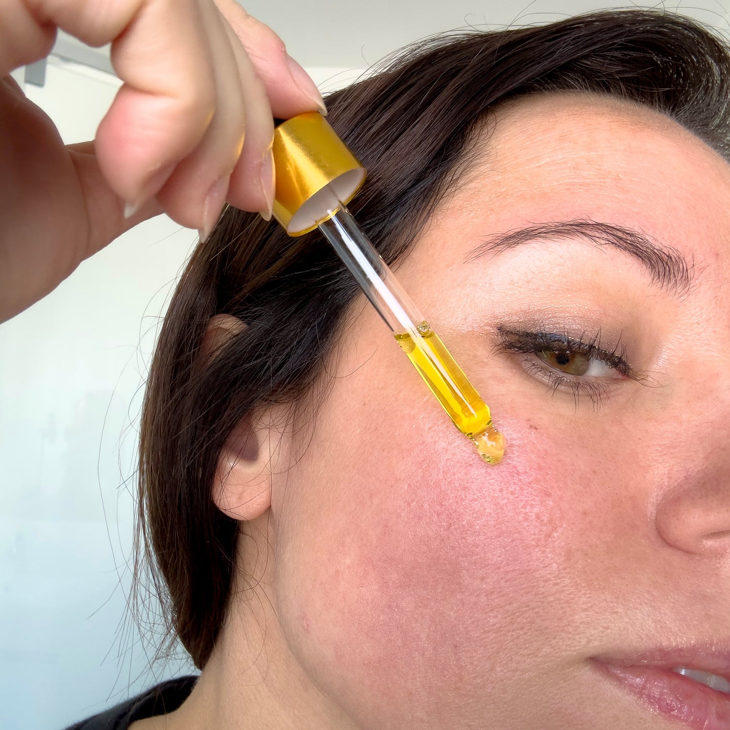 Person applying a dropper of yellow liquid to their face