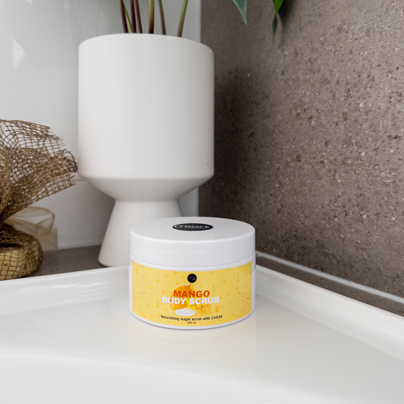 Jar of mango body scrub on a surface with a plant in the background