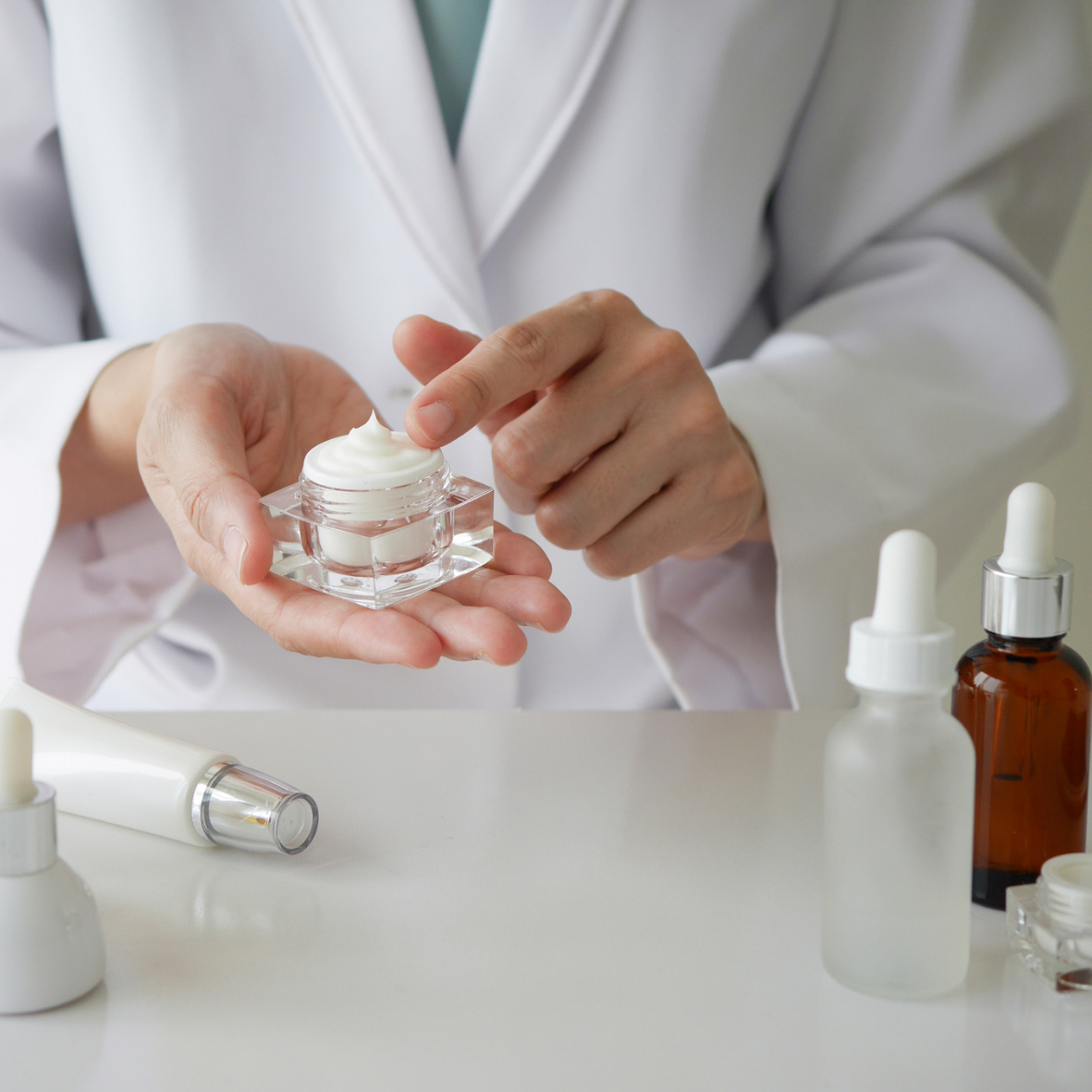 Person holding a jar of cream with skincare products on a table